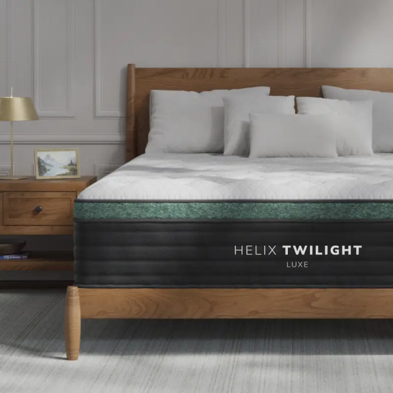 Helix Twilight Luxe mattress featuring GlacioTex™ cooling cover and premium quilted pillow top, positioned on a wooden bed frame with decorative pillows and a bedside table.