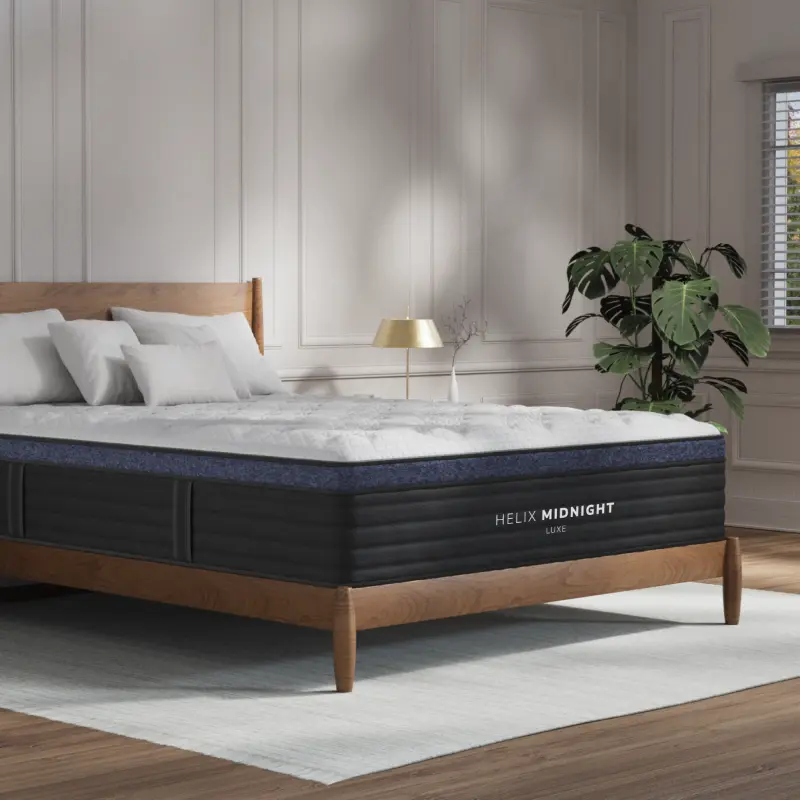 Helix Midnight Luxe mattress on a wooden bed frame, featuring a plush pillow top and cooling cover, surrounded by a modern room decor with a plant and lamp.