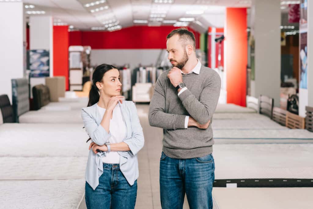 pensive couple looking at each other in furniture store with arranged mattresses