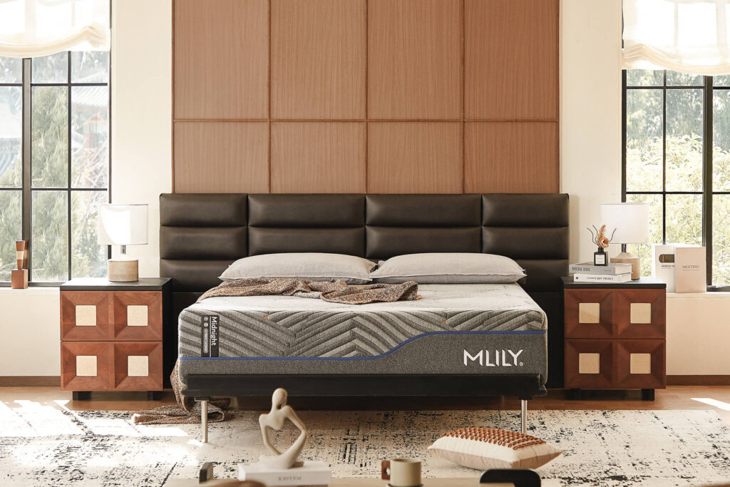 MLILY Midnight 1.0 Hybrid Mattress displayed on a modern bed frame with a black upholstered headboard, surrounded by stylish nightstands and decorative elements in a well-lit bedroom setting.