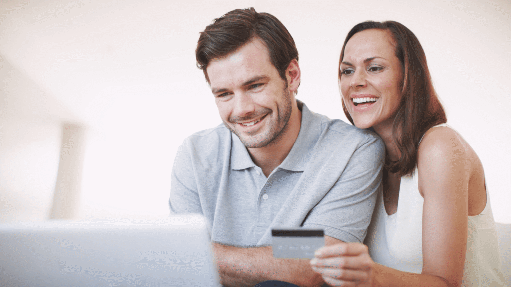 Couple smiling while using a laptop and holding a credit card, representing online financing options for purchasing a mattress.
