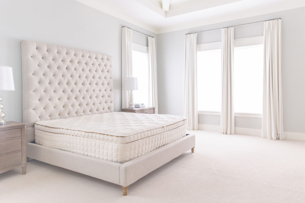 Organic mattress on a stylish bed frame in a bright, modern bedroom with a tufted headboard and elegant decor, highlighting customizable comfort and non-toxic materials.
