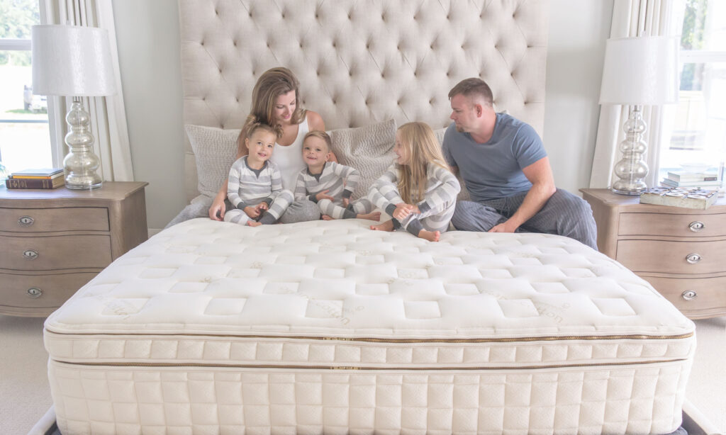 Family enjoying time on a Naturepedic organic mattress, featuring a plush pillowtop design, in a bright bedroom setting with a stylish headboard and bedside tables.
